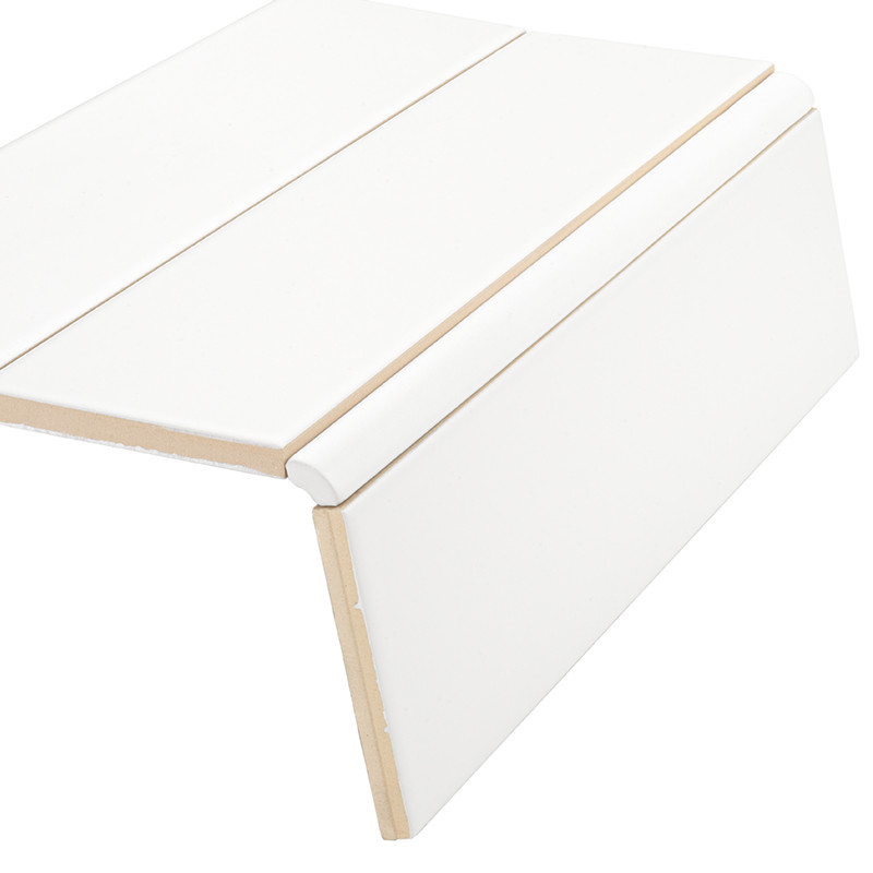 Azulejo blanco rectangular con perfil en L y juntas visibles, acabado liso; colocado como remate de escalón o panel sobre fondo neutro blanco.