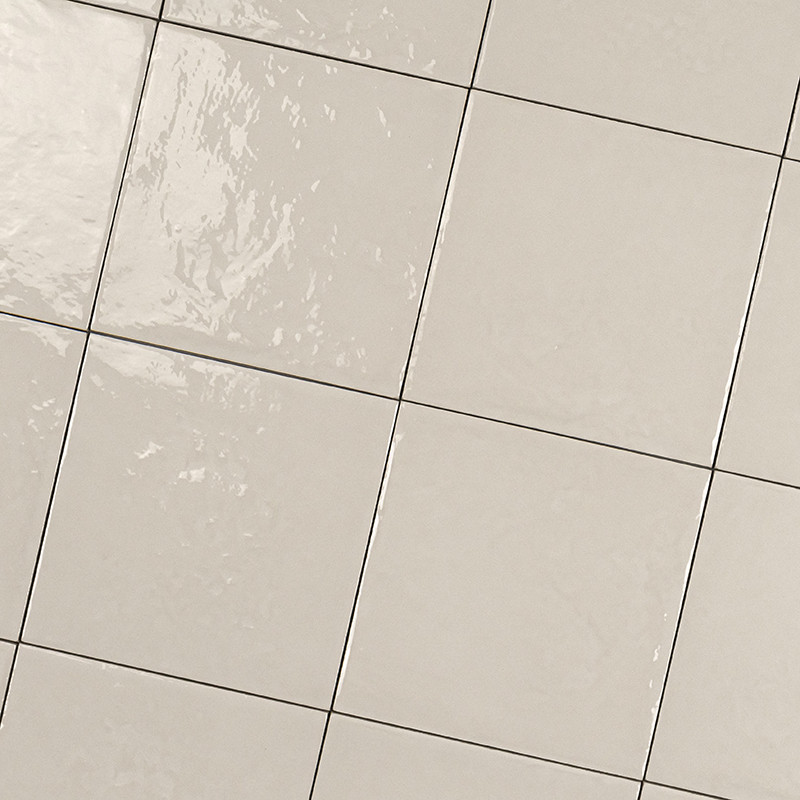 Azulejo cerâmico quadrado creme brilhante com rejunte escuro; superfície apresenta reflexos de luz, provavelmente piso ou revestimento de parede em banheiro ou cozinha.