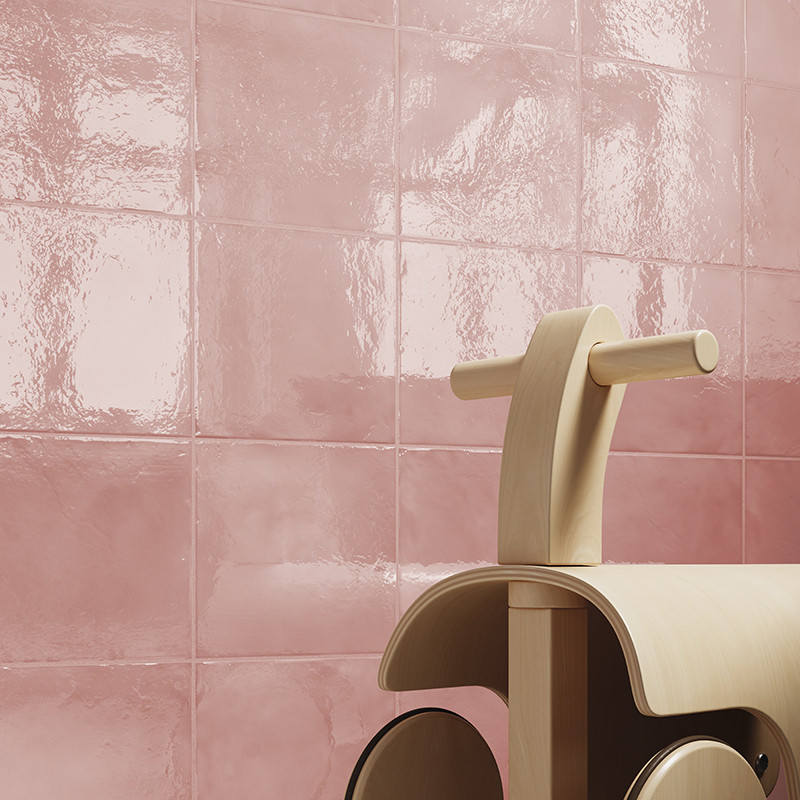 Carrelage rose brillant, carreaux carrés à joints visibles et reflets vernissés; au premier plan, jouet en bois minimaliste (trottinette/cheval) partiellement visible.