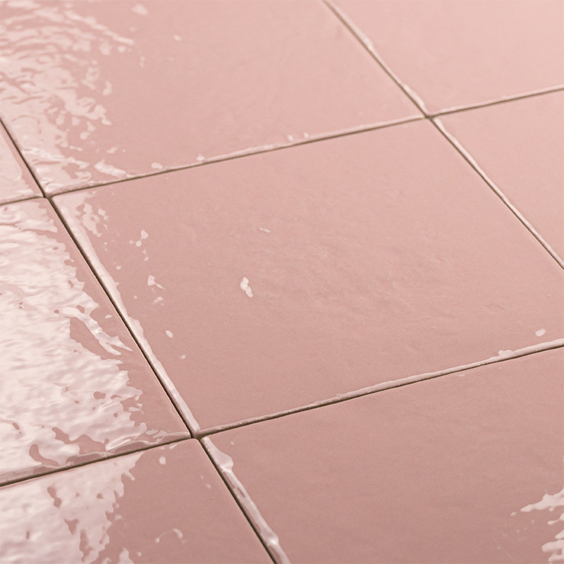 Carrelage rose saumon brillant, carreaux carrés aux joints blancs; surface humide avec reflets et petites gouttes d'eau.