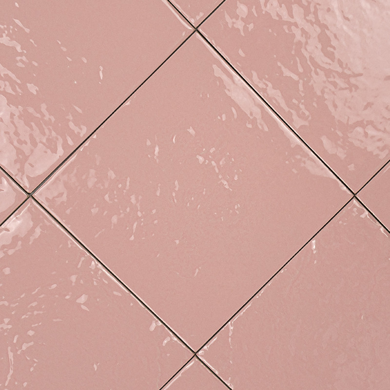 Azulejo cerâmico quadrado rosa, disposto em diagonal; rejunte fino escuro; superfície brilhante com reflexos irregulares e pequenas ondulações na esmaltação.