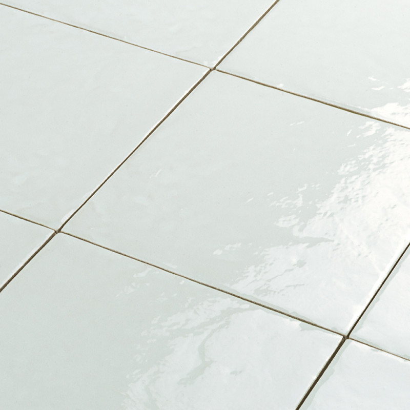 Carrelage blanc brillant, dalles carrées aux joints fins beiges, surface légèrement ondulée et réfléchissante indiquant un fini vernissé, sol intérieur bien éclairé.
