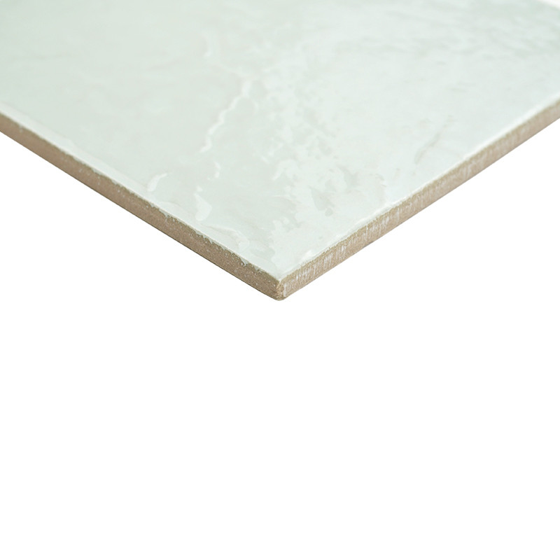 Azulejo cerámico blanco crema con brillo esmaltado y canto biselado, esquina en primer plano, fondo neutro blanco que lo aísla del entorno.