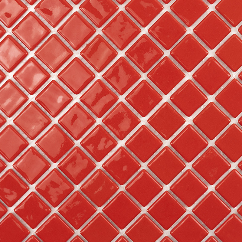 Azulejos rojos pequeños dispuestos en líneas diagonales, separados por juntas claras; superficie vidriada y brillante con reflejos irregulares.