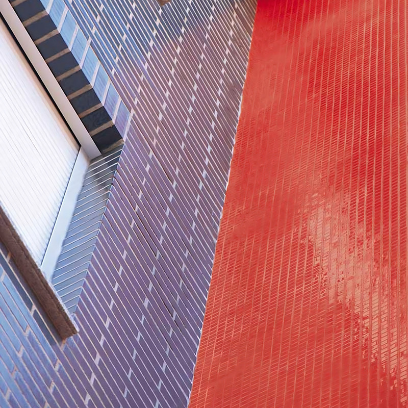Azulejo vermelho brilhante à direita; parede de azulejos azul-acinzentados à esquerda com janela estreita inclinada; perspectiva vertical realçando a junção entre as superfícies.