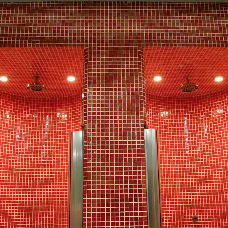 Bright red mosaic tile; two recessed showers with metal shower heads, curved niches and vertical steel handles, recessed ceiling lighting.