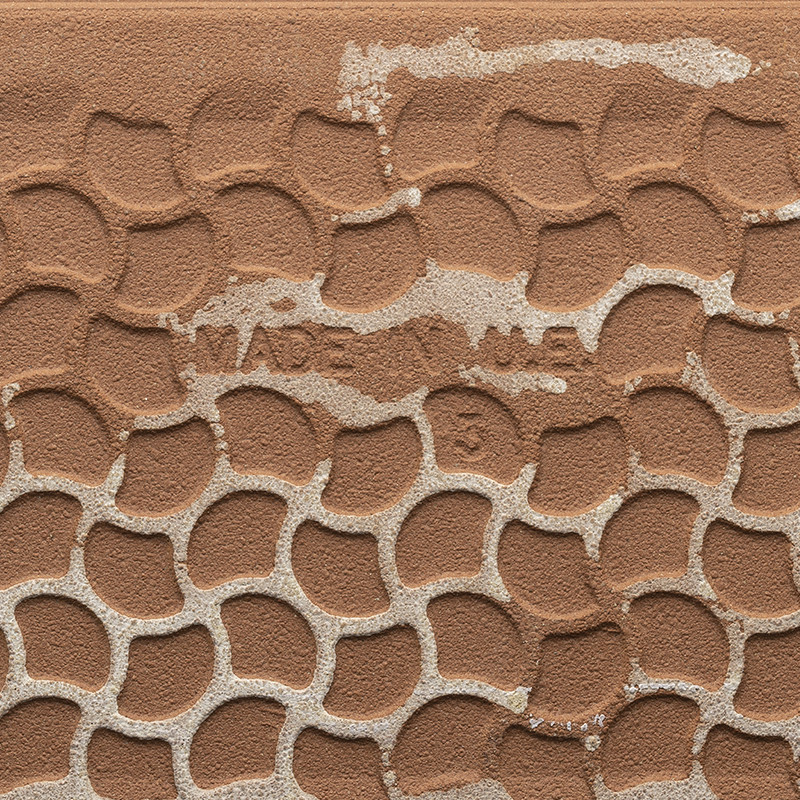 Clay tile with a repeating pattern of raised semicircles; cracked and chipped surface showing light grout. Visible text: "MADE IN [illegible]".