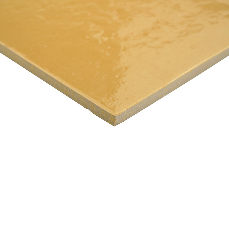Carreau rectangulaire jaune moutarde à surface légèrement brillante; arête effilée visible, face inférieure beige, posé en angle sur fond blanc neutre.