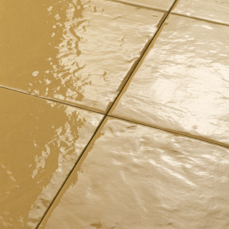 Carrelage beige brillant à joints visibles, plusieurs dalles carrées légèrement bosselées; surface humide réfléchissante suggère présence d'eau ou d'éclats lumineux.