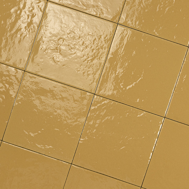 Square beige ceramic tiles, glossy surface with reflections and irregular texture; thin black joints forming a grid, perspective on an inclined plane of the floor.