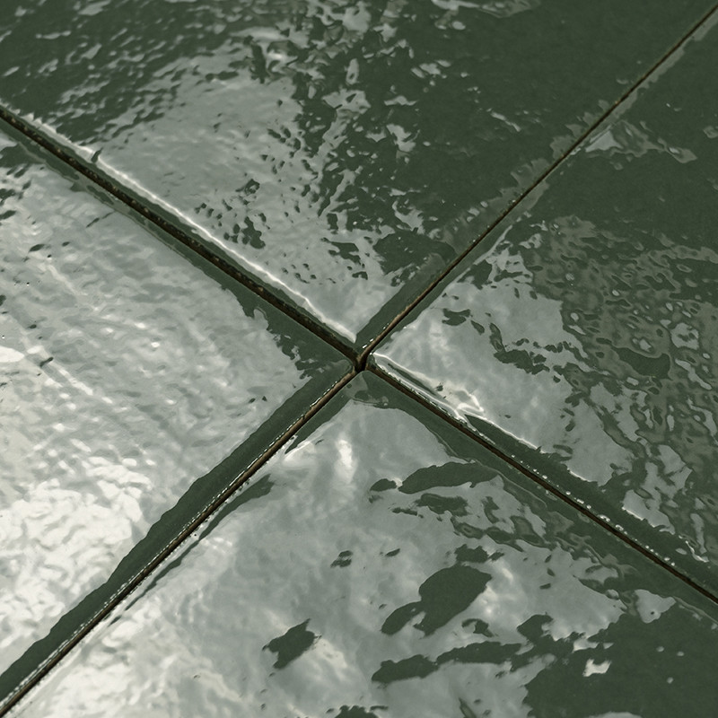 Carrelage en faïence vert foncé, joints minces et sombres formant une croix, surface brillante aux reflets mouillés, gros plan sur l'intersection de quatre carreaux.