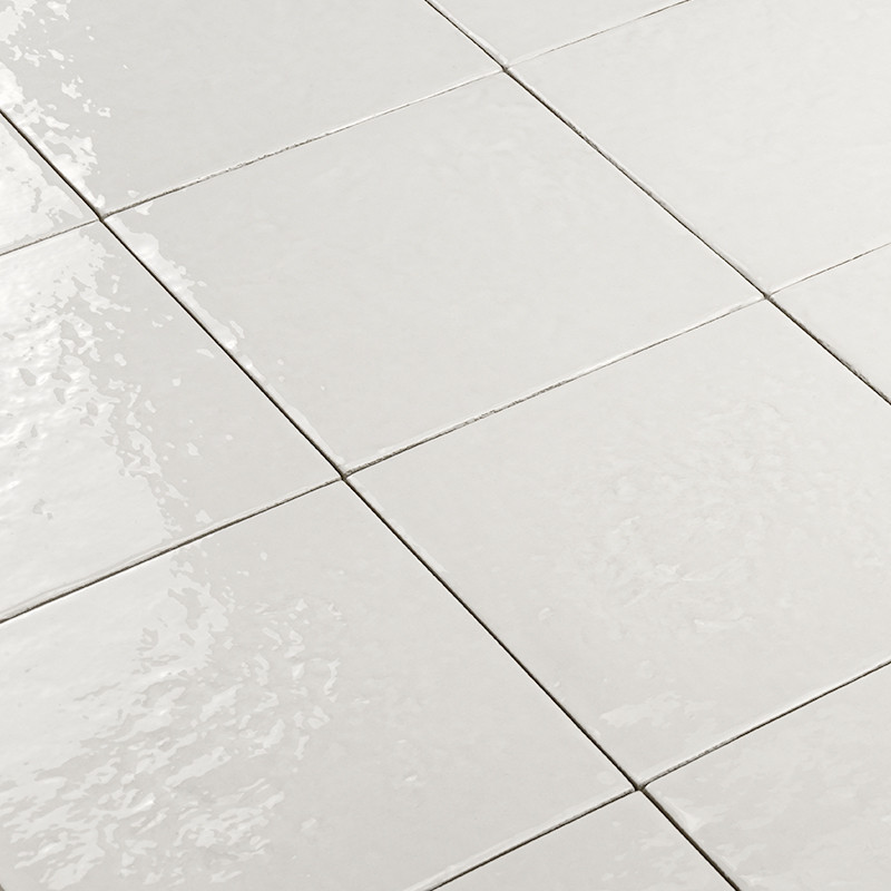Azulejo cerámico blanco brillante en patrón de rejilla; juntas finas y reflejos de luz sobre un suelo liso.