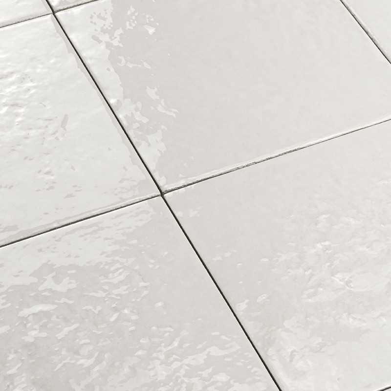 Carrelage blanc brillant à grandes dalles carrées, joints gris fins, surface légèrement ondulée avec reflets lumineux, formant un sol intérieur lisse.