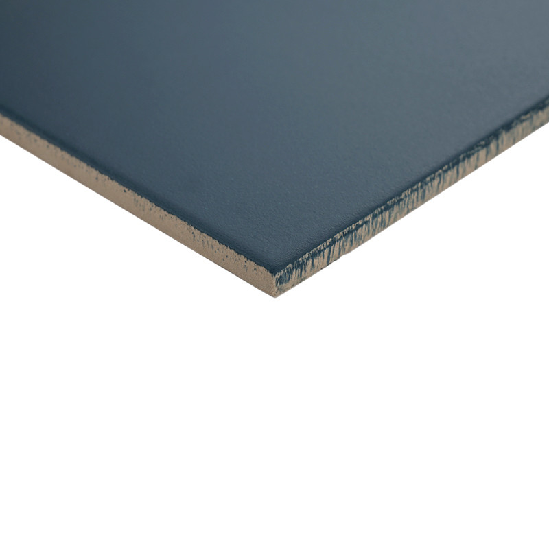 Carreau céramique bleu mat, coupe oblique montrant épaisseur et noyau beige; bords légèrement usés, posé sur fond blanc uni.