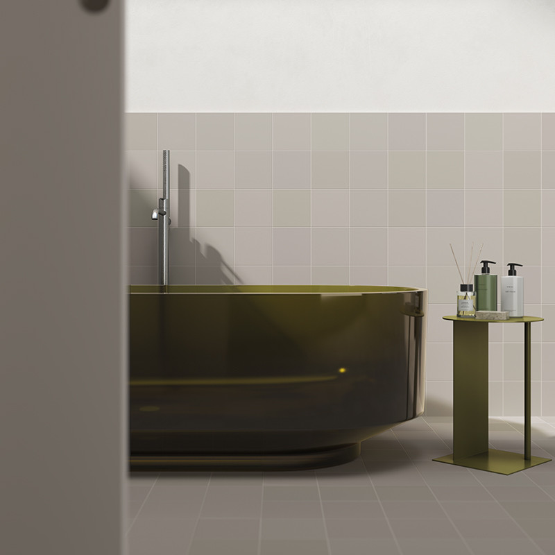 Oval olive green bathtub in the foreground; wall and floor with light gray square tiles, minimalist faucet and side table with dispensers and glass.