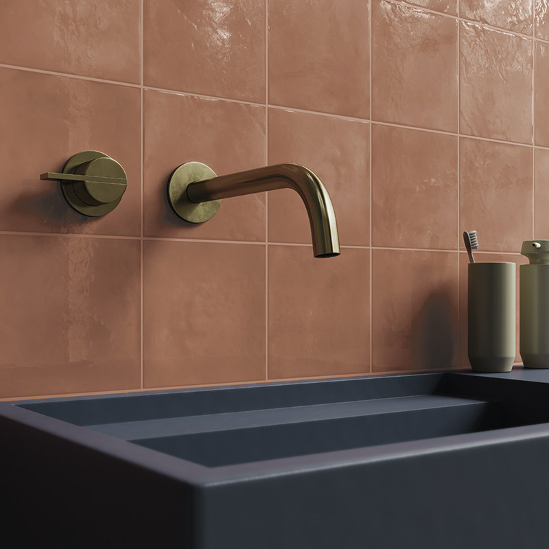 Carrelage carré saumon lustré couvrant le mur; robinet mural en laiton, évier rectangulaire bleu foncé et gobelet contenant une brosse à dents sur le rebord.