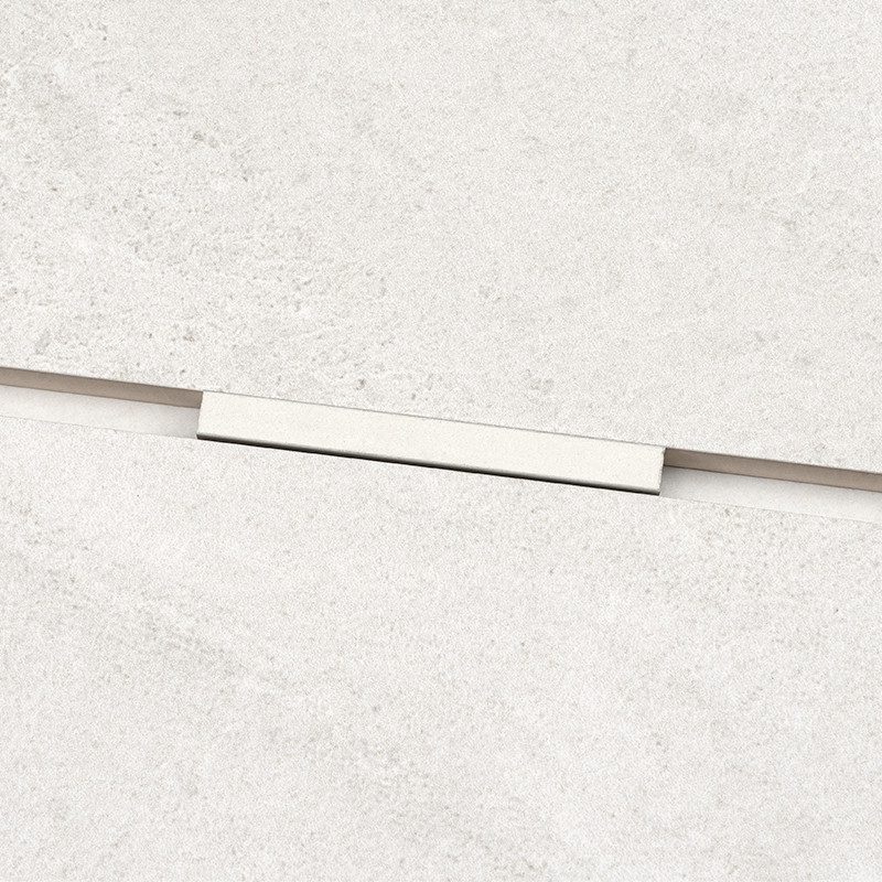 Profilé rectangulaire blanc posé sur le joint entre deux carreaux crème, entouré d'une surface carrelée texturée claire.