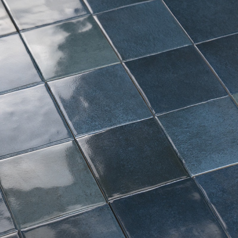 Azulejos cuadrados azul oscuro, acabado esmaltado y brillante; juntas finas, suaves reflejos de luz y nubes sobre la superficie, dispuestos en patrón cuadriculado.