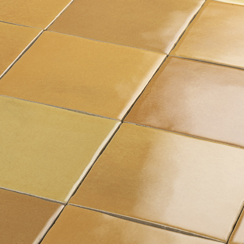Azulejos cerámicos cuadrados brillantes color ocre, dispuestos en rejilla con juntas visibles; superficie reflectante muestra ligeros reflejos y variaciones de tono.