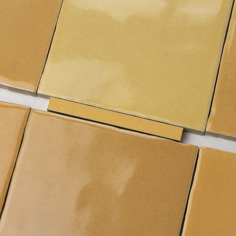 Square glossy beige ceramic tile; white grout between pieces and rectangular yellow spacer in the center, arranged in a continuous pattern.
