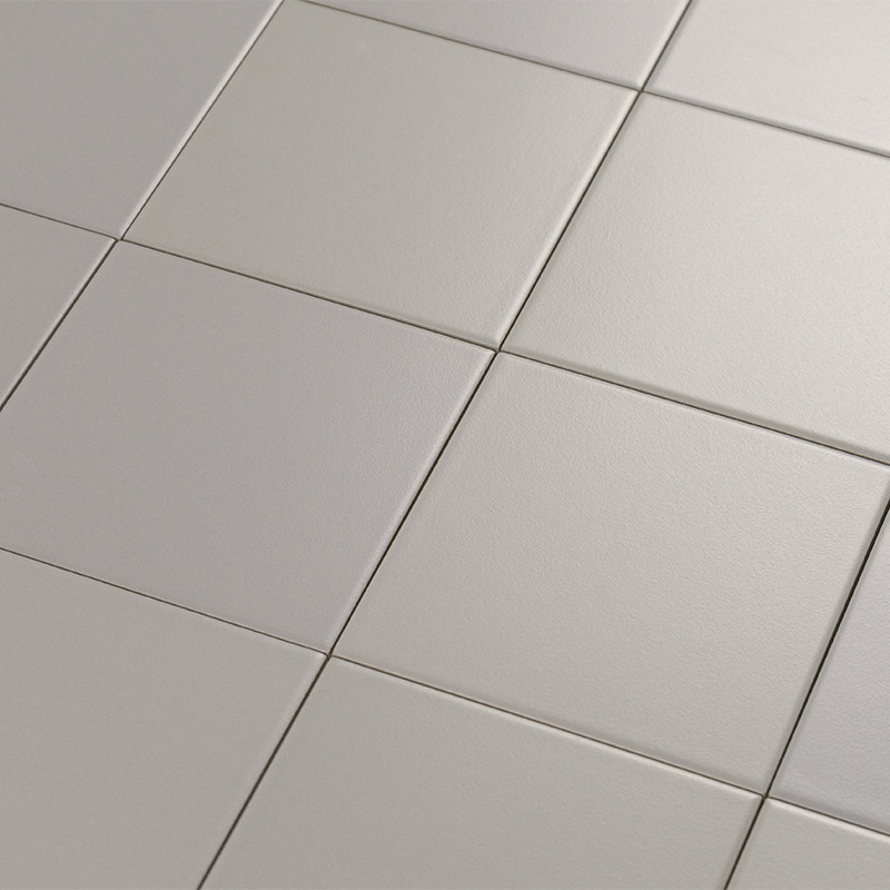 Azulejo cerámico cuadrado liso color beige claro, dispuesto en rejilla con juntas finas, rodeado por azulejos similares con ligero brillo y textura sutil.