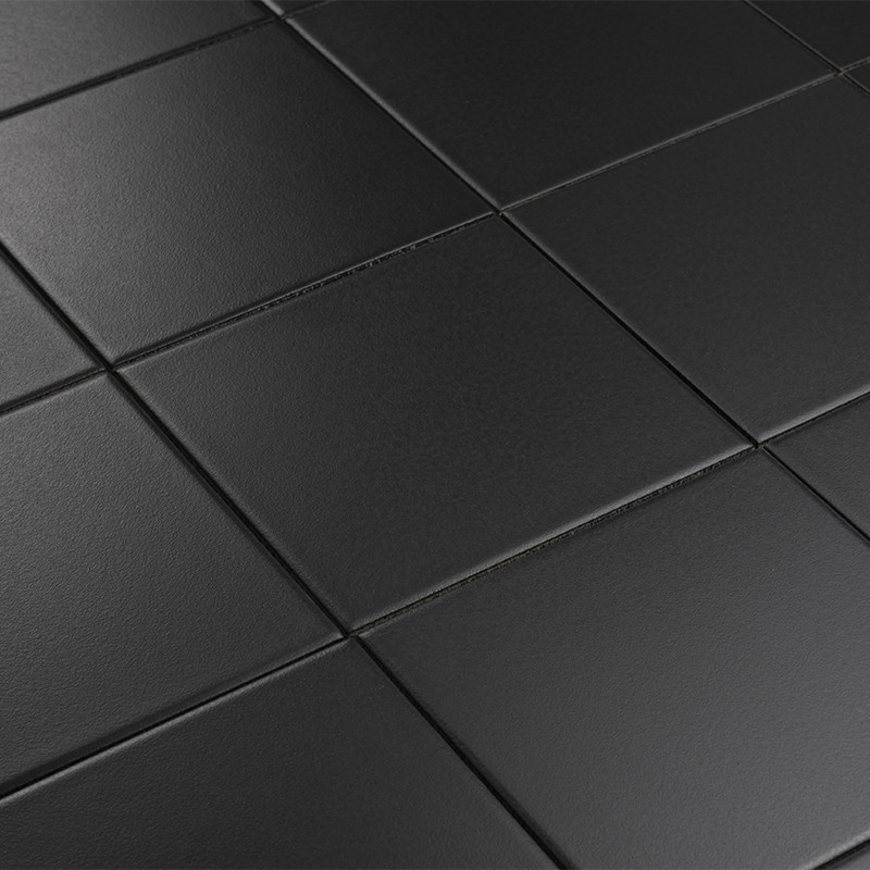 Carrelage noir mat composé de carreaux carrés aux joints fins; surface légèrement texturée et réfléchissante, perspective oblique révélant plusieurs rangées.