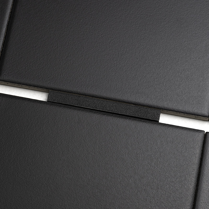 Carrelage noir mat rectangulaire en gros plan; joint central avec entretoise noire et fines lignes de mortier blanc, surface légèrement texturée.