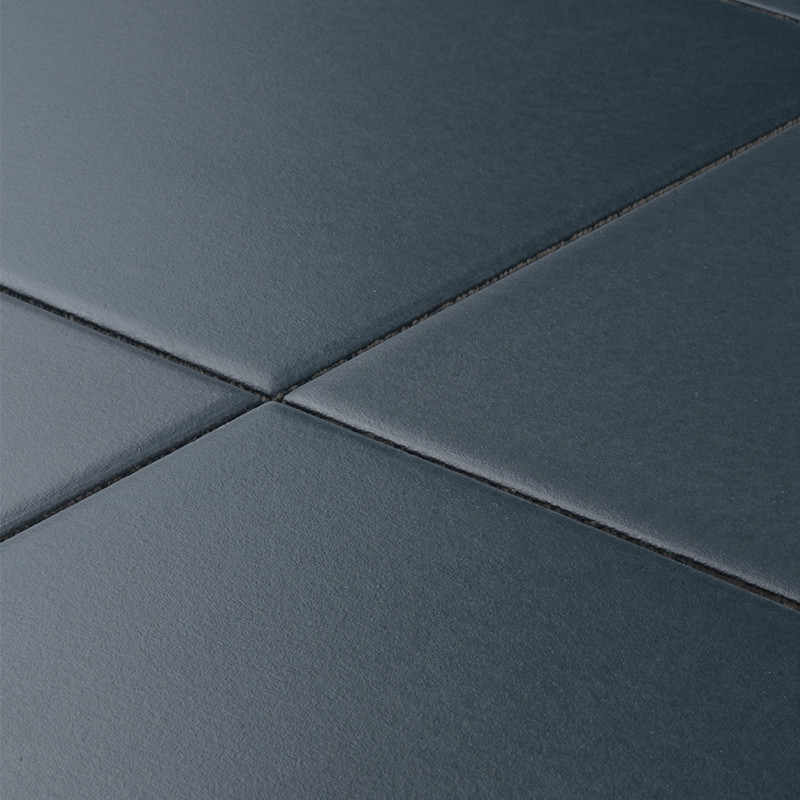 Carrelage carré gris anthracite mat, joints fins formant une croix; surface légèrement texturée, éclairage doux créant reflets et ombres.