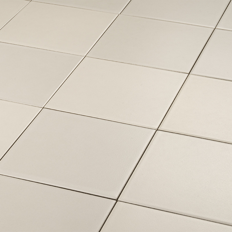 Beige, quadratische Keramikfliesen in regelmäßigem Raster; sichtbare schmale Fugen, leicht glänzende, glatte Oberfläche, perspektivische Anordnung mit Schatten entlang der Kanten.
