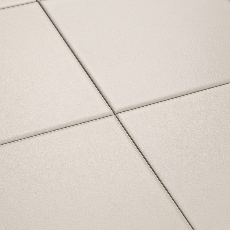 Azulejos quadrados beges foscos; quatro peças se encontram formando uma cruz de rejunte, superfície levemente texturizada vista em ângulo oblíquo.