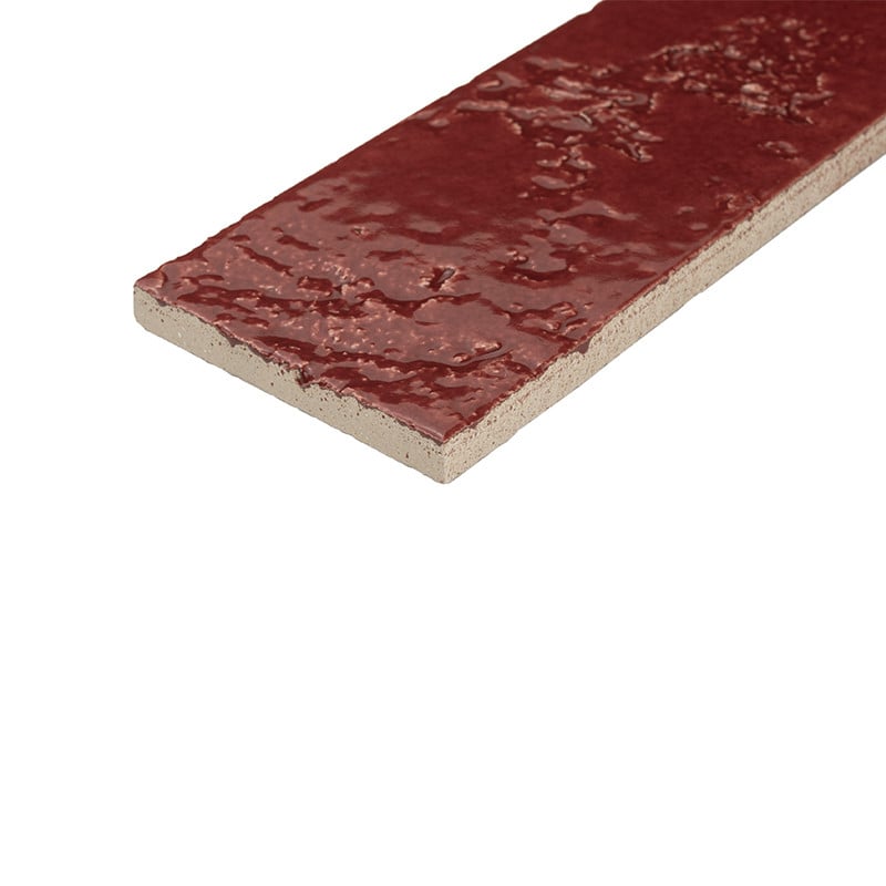 Azulejo rectangular delgado color rojo brillante con superficie esmaltada y texturada; borde de gres beige visible; colocado en ángulo sobre fondo blanco liso.