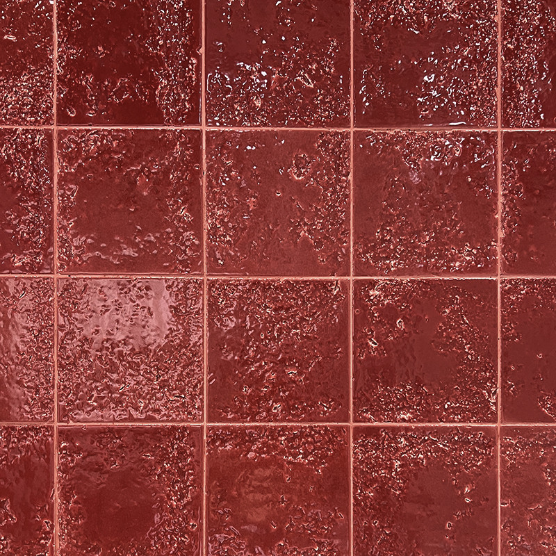 Carrelage rouge brique brillant: carreaux carrés texturés, joints fins formant une grille régulière, surface irrégulière et luisante reflétant la lumière.
