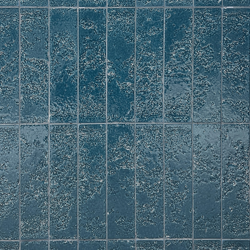 Carrelage bleu-vert rectangulaire à joints clairs, surface texturée et mouchetée, disposé en grille régulière couvrant un mur ou un sol.