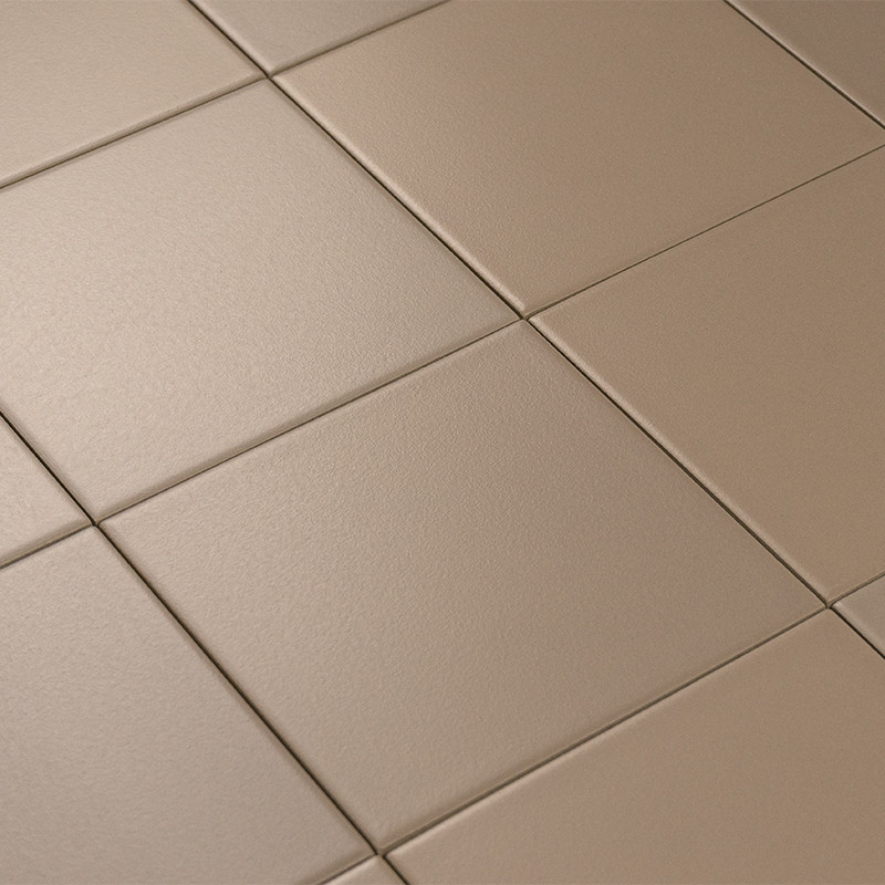 Carrelage beige mat, grands carreaux carrés avec joints en creux; surface légèrement texturée, vue en plongée montrant plusieurs dalles sous éclairage doux.