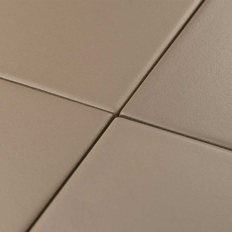 Carrelage beige: quatre carreaux se rencontrent en croix, joints fins légèrement plus foncés, surface mate et granuleuse, perspective rapprochée centrée sur l'angle de jonction.
