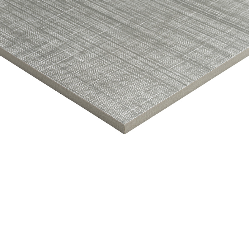 Azulejo rectangular gris con textura de trama cruzada en primer plano; vista de su canto y esquina elevada sobre fondo blanco neutro.