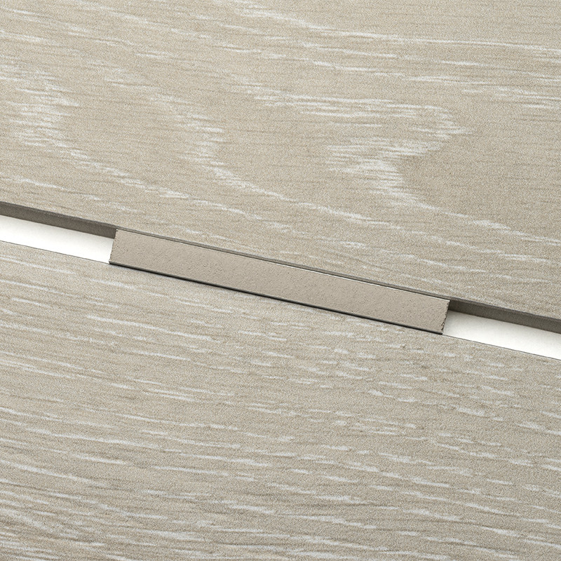 Smalle rechthoekige metalen voegstrip op een lichte houtlooktegel, geplaatst in de naad tussen twee tegels; zichtbare houtnerf en matte, beige-achtige afwerking.