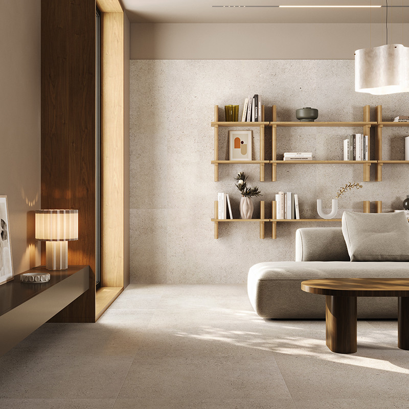Carrelage grand format beige clair au sol; salon lumineux avec canapé modulable gris, table basse ronde en bois, étagères murales minimalistes, lampe sur console et forte lumière naturelle.