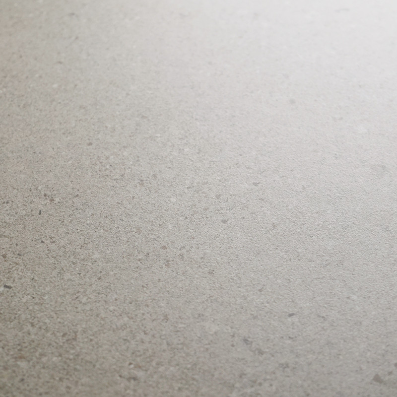 Carrelage beige granuleux, surface mate et uniforme; légères tâches et grains; occupe tout le cadre; éclairage doux depuis le coin supérieur droit.