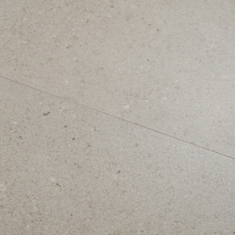 Baldosa beige claro con pequeñas motas y una línea fina diagonal (junta o grieta); superficie mate y continua que sugiere más baldosas adyacentes.