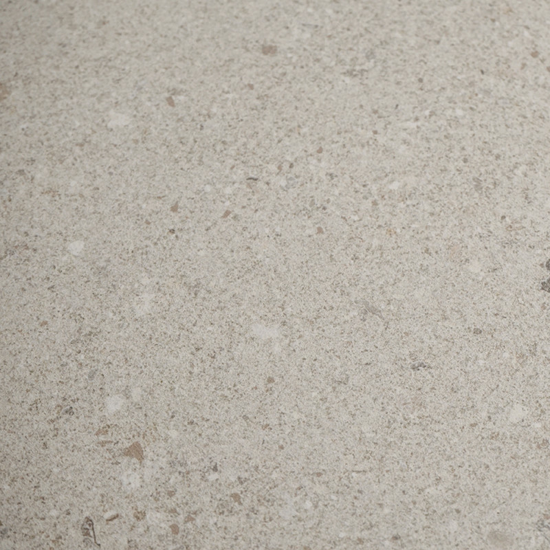 Azulejo crema de piedra con textura granular y pequeñas motas blancas y marrones; se ve extendido en un plano uniforme sin juntas ni elementos vecinos.