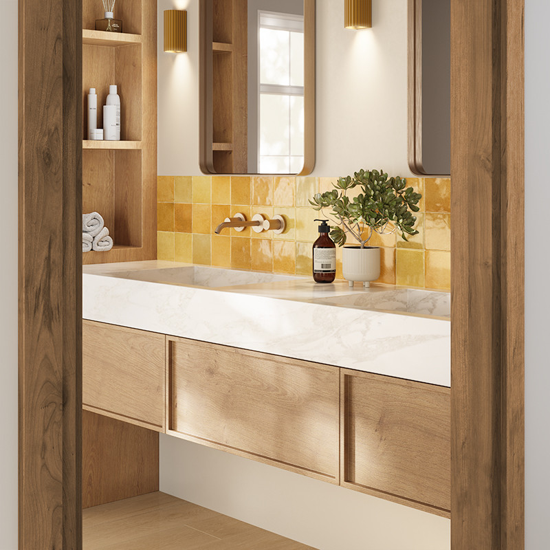 Carrelage mural jaune carré, devant une vasque encastrée marbrée; meuble-lavabo en bois clair, miroir vertical, étagères ouvertes avec serviettes, flacon et plante en pot.