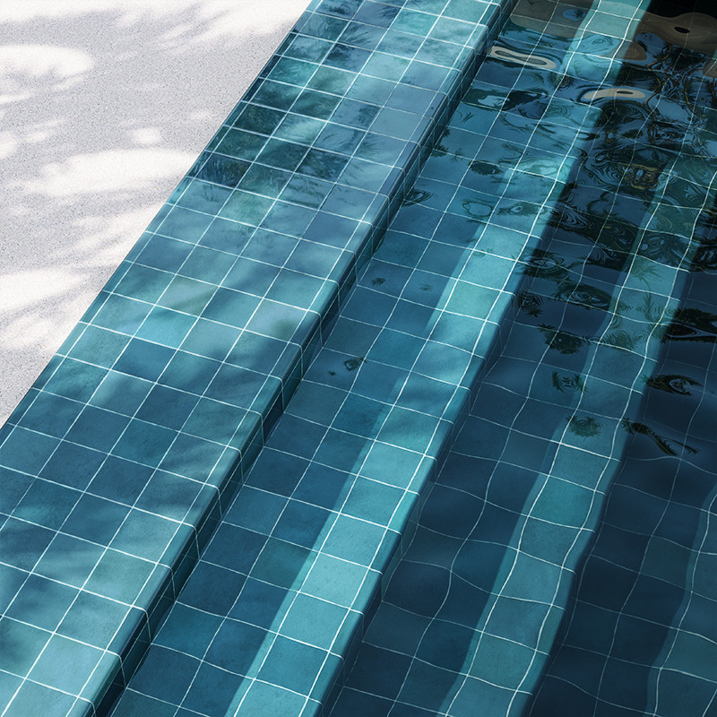 Carrelage de piscine bleu-vert en petites dalles carrées, marches immergées aux reflets ondulants, bord en béton clair avec ombres d'arbres.