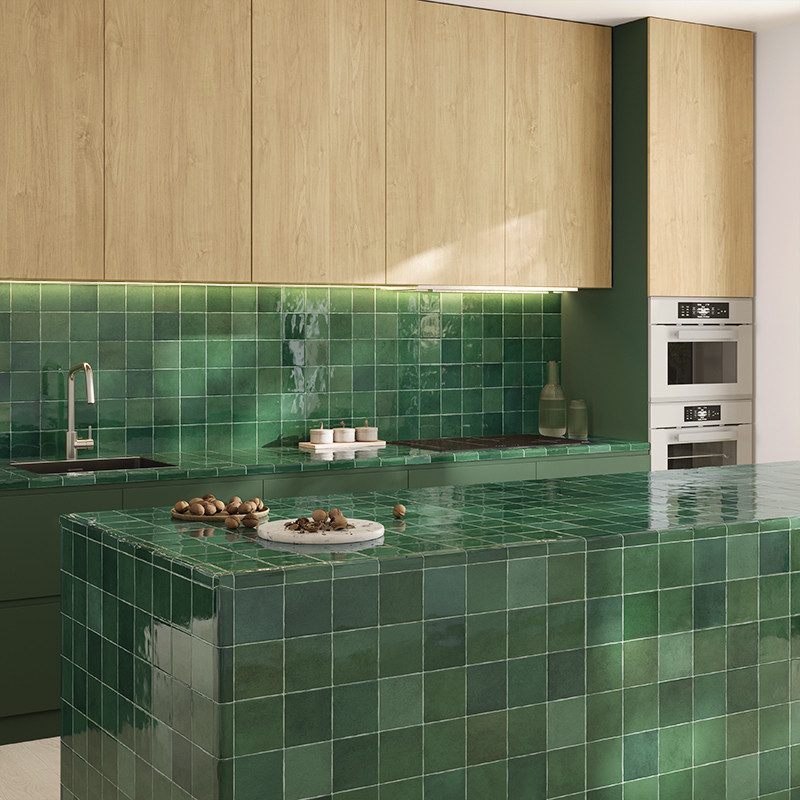 Groene geglazuurde vierkante tegels bedekken kookeiland en achterwand; keuken met licht houten bovenkasten, ingebouwde ovens, RVS kraan en minimalistische, goed verlichte werkruimte.
