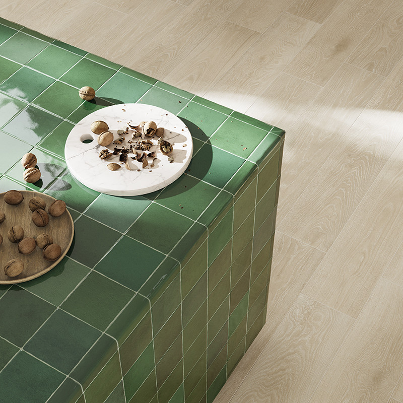 Block covered in bright green tiles; on top, two plates with nuts and shells; surroundings: light laminate flooring and side sunlight.