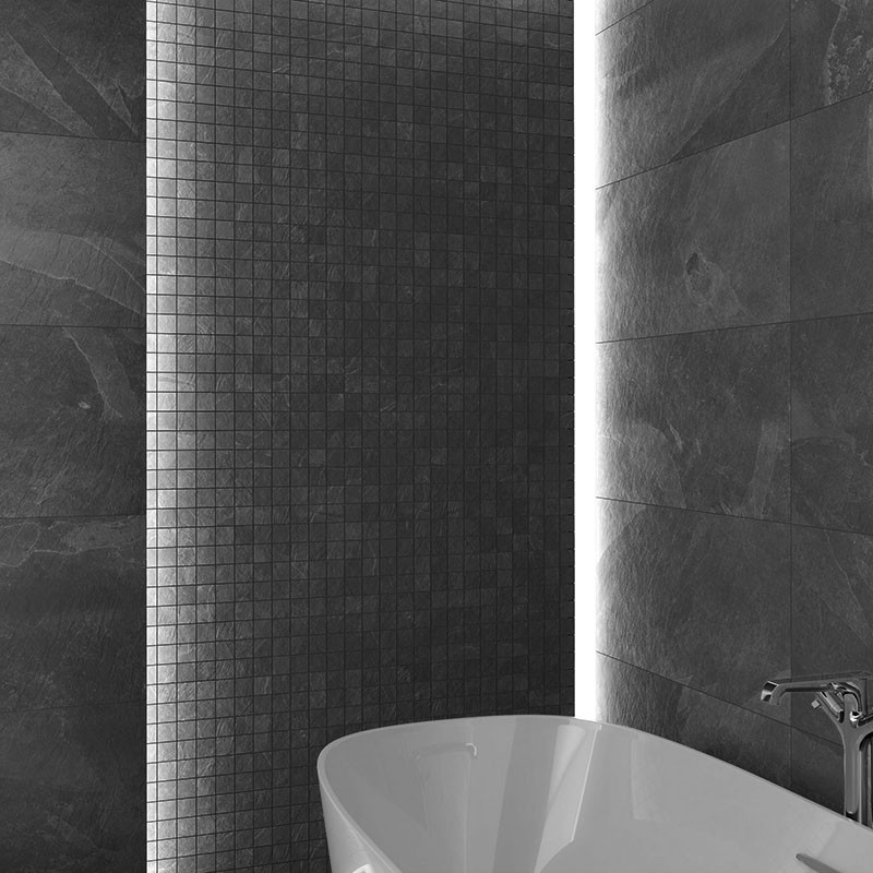 Carrelage mural de mosaïque carrée sombre; baignoire îlot blanche partiellement visible devant un mur en grandes dalles anthracite, éclairage vertical lumineux et robinet chromé.