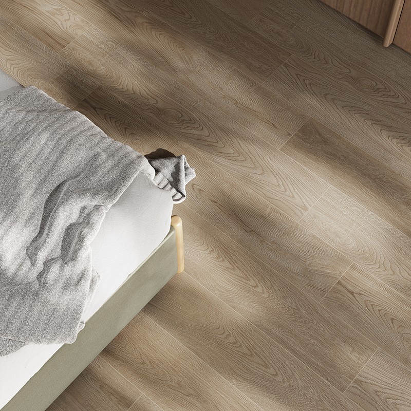 Holzoptik-Fliese in warmem Beige, am Fuß eines Bettes mit weißer Matratze und grauem Stricküberwurf; seitlich einfallendes Licht und weiche Schatten.