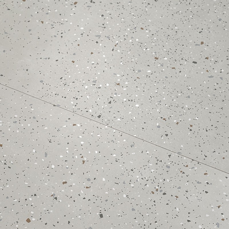 Hellgraue Terrazzo-Fliese mit kleinen weißen, grauen und braunen Einsprengseln; dünne dunkle Fuge verläuft diagonal über die Oberfläche.