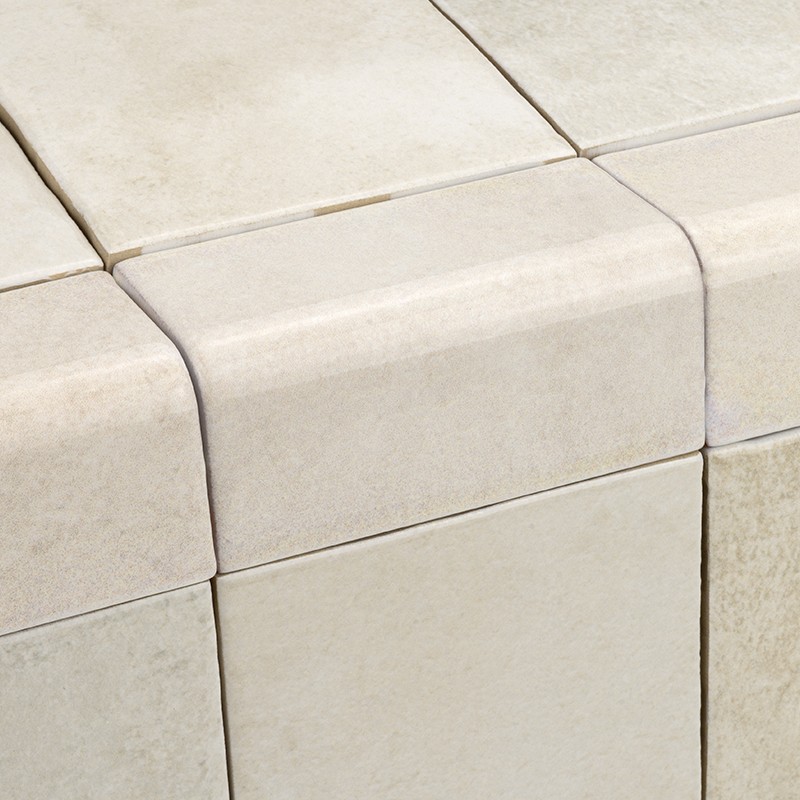 Creamy white ceramic tile with rounded edge; placed in corner of set of similar tiles, thin joints visible and slightly porous matte texture.