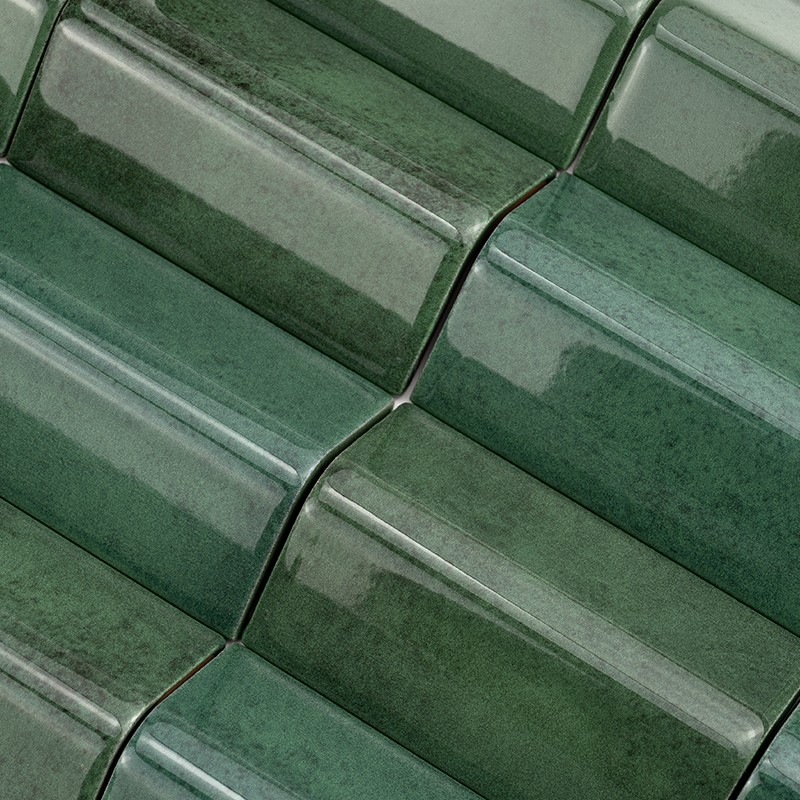Azulejo cerámico esmaltado verde, piezas alargadas y biseladas; dispuestas en patrón escalonado sobre pared, brillo reflectante y leves variaciones tonales.
